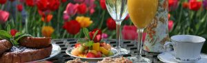 Breakfast food and drink items on a table with multi-colored tulips in the background.