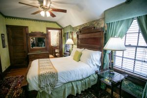 Guest room with green walls and a multi-colored rug. Green curtains drape the windows.