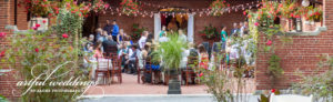 Outdoor reception with people sitting in a bricked courtyard and plants are all around.