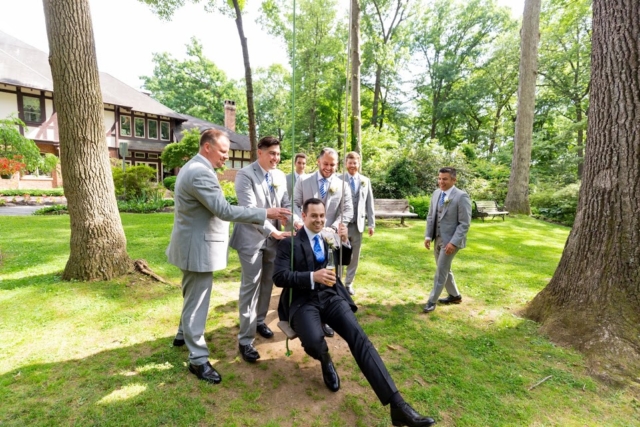 Men in gray suits pushing the groom on a swing outside.