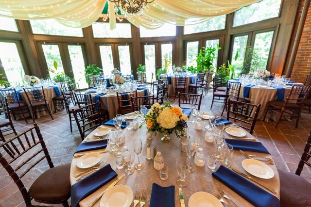 Indoor reception space with brown chairs, white table linens and blue napkins.