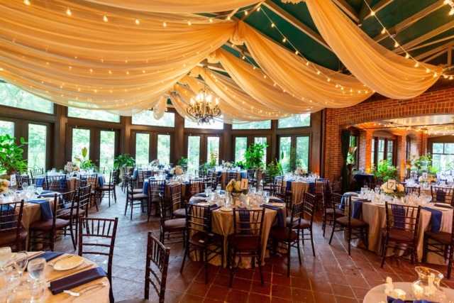Indoor reception space with champagne colored ceiling draping, lights and tables and chairs.