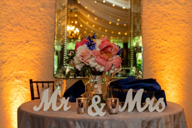 Mr. and Mrs. Sweetheart table with blue linens, flowers and golden light next to a mirror.