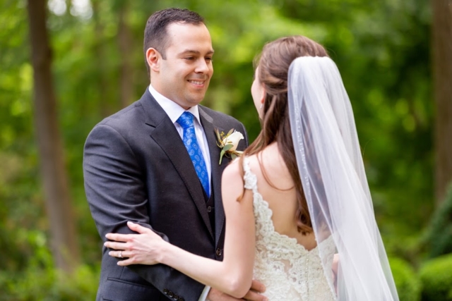 Bride and groom standing in the gardens. The groom is in a gray suit and the bride is in a white dress with veil.