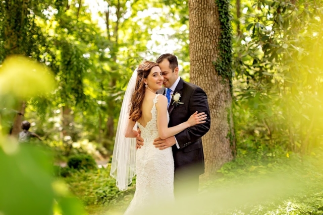 Bride and groom smiling behind plants in the garden.